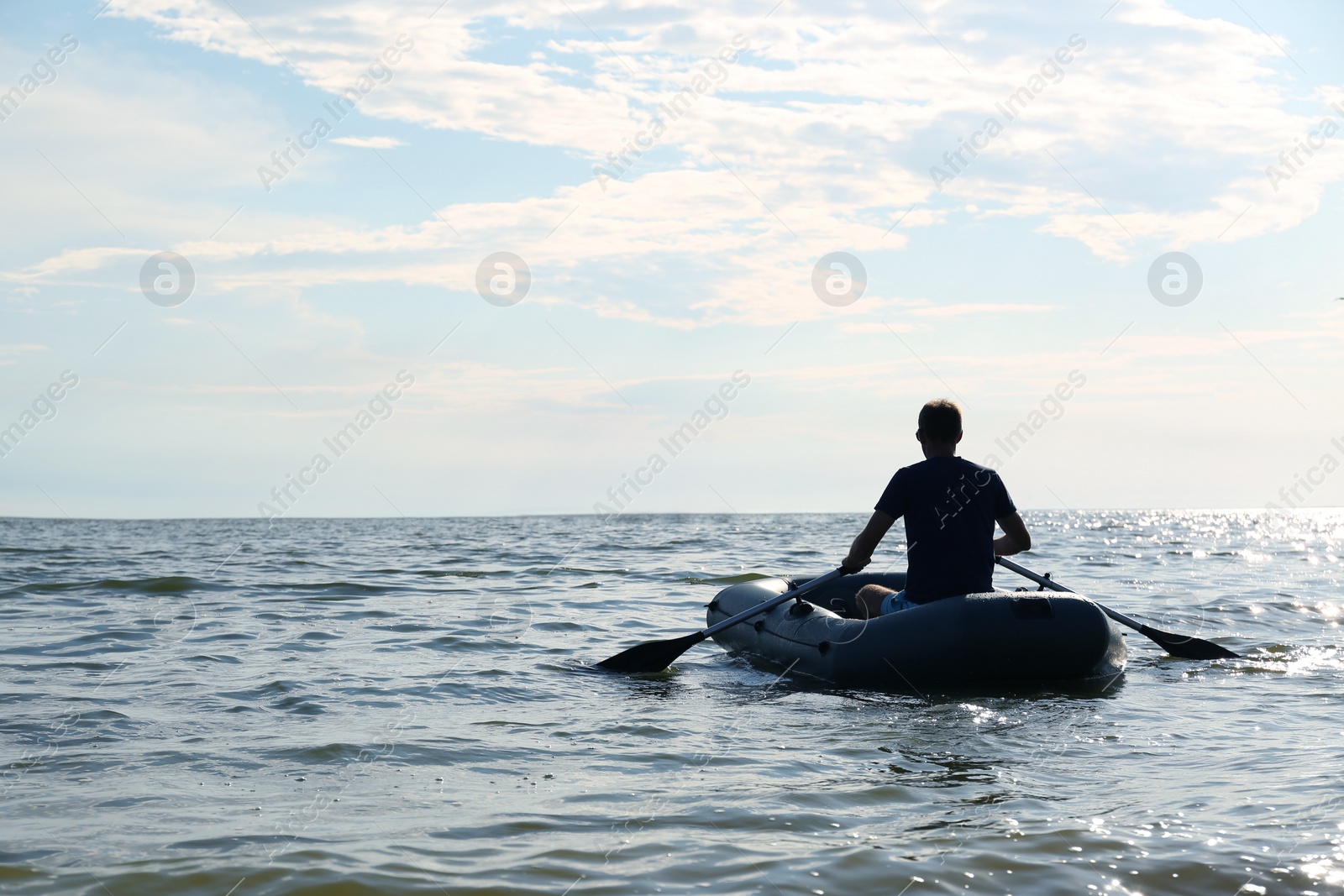 Photo of Man rowing inflatable rubber fishing boat on sea, back view. Space for text