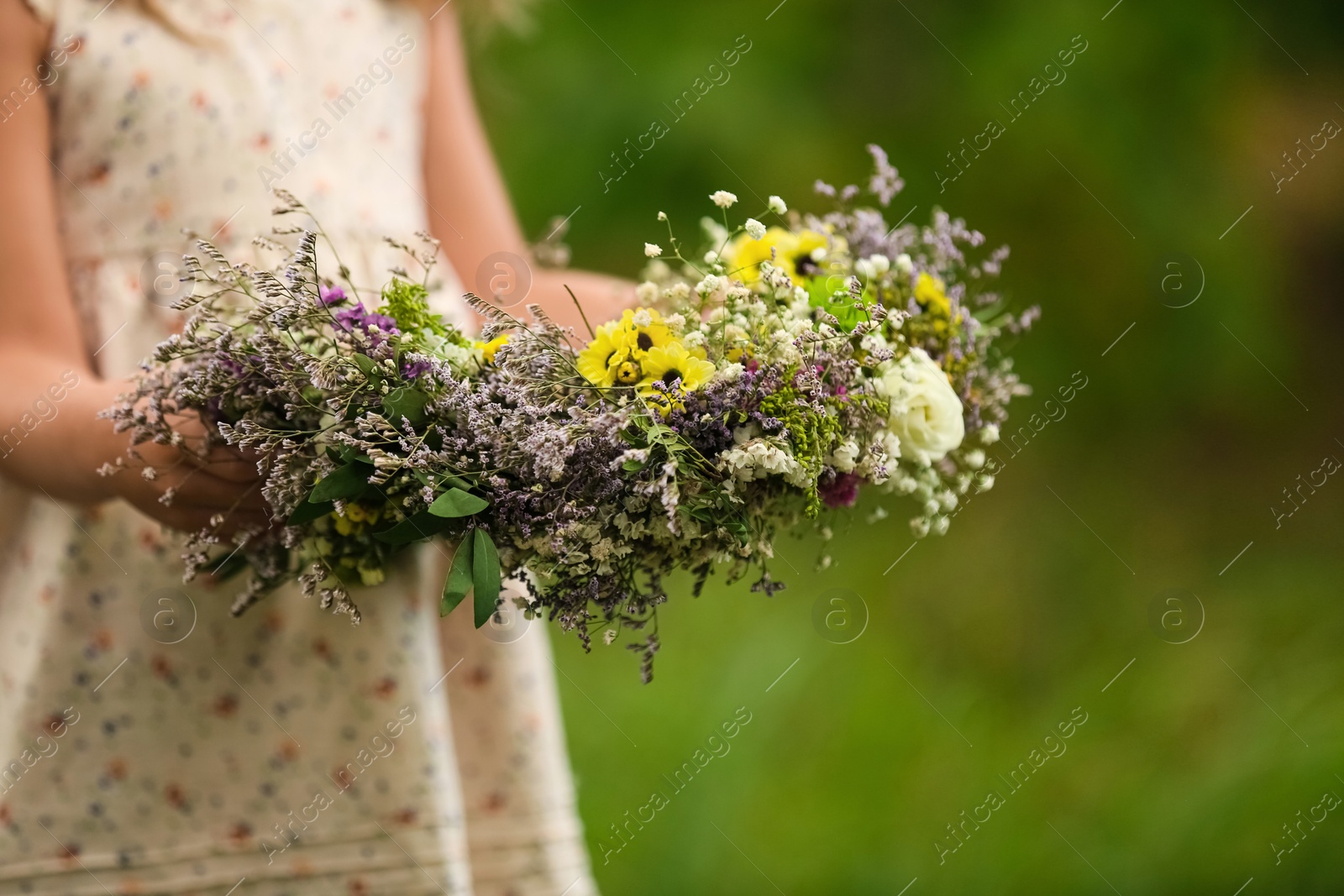 Photo of Cute little girl holding wreath made of beautiful flowers outdoors, closeup