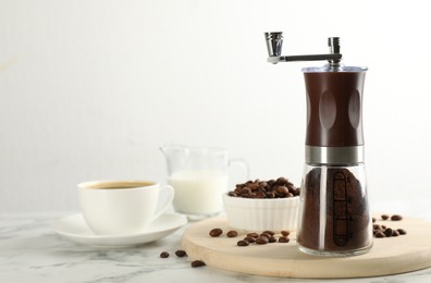 Photo of Manual coffee grinder with powder, beans and cup of drink on white marble table