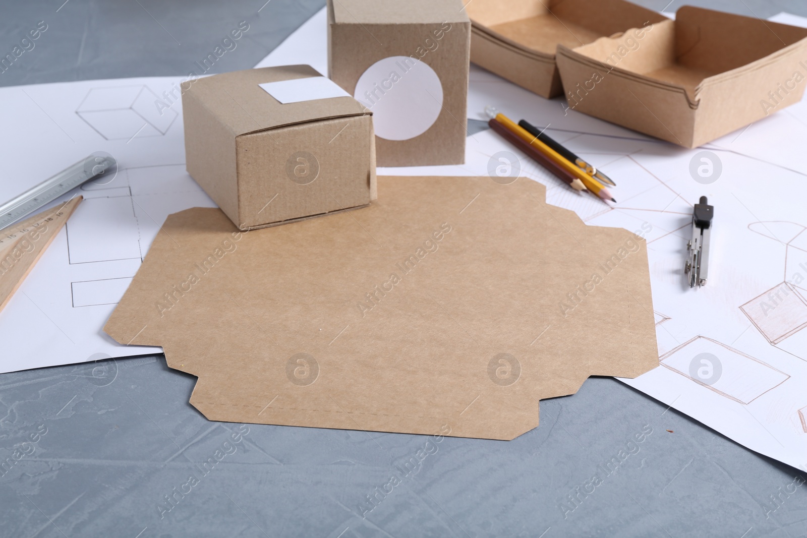 Photo of Creating packaging design. Drawings, boxes and stationery on blue textured table, closeup