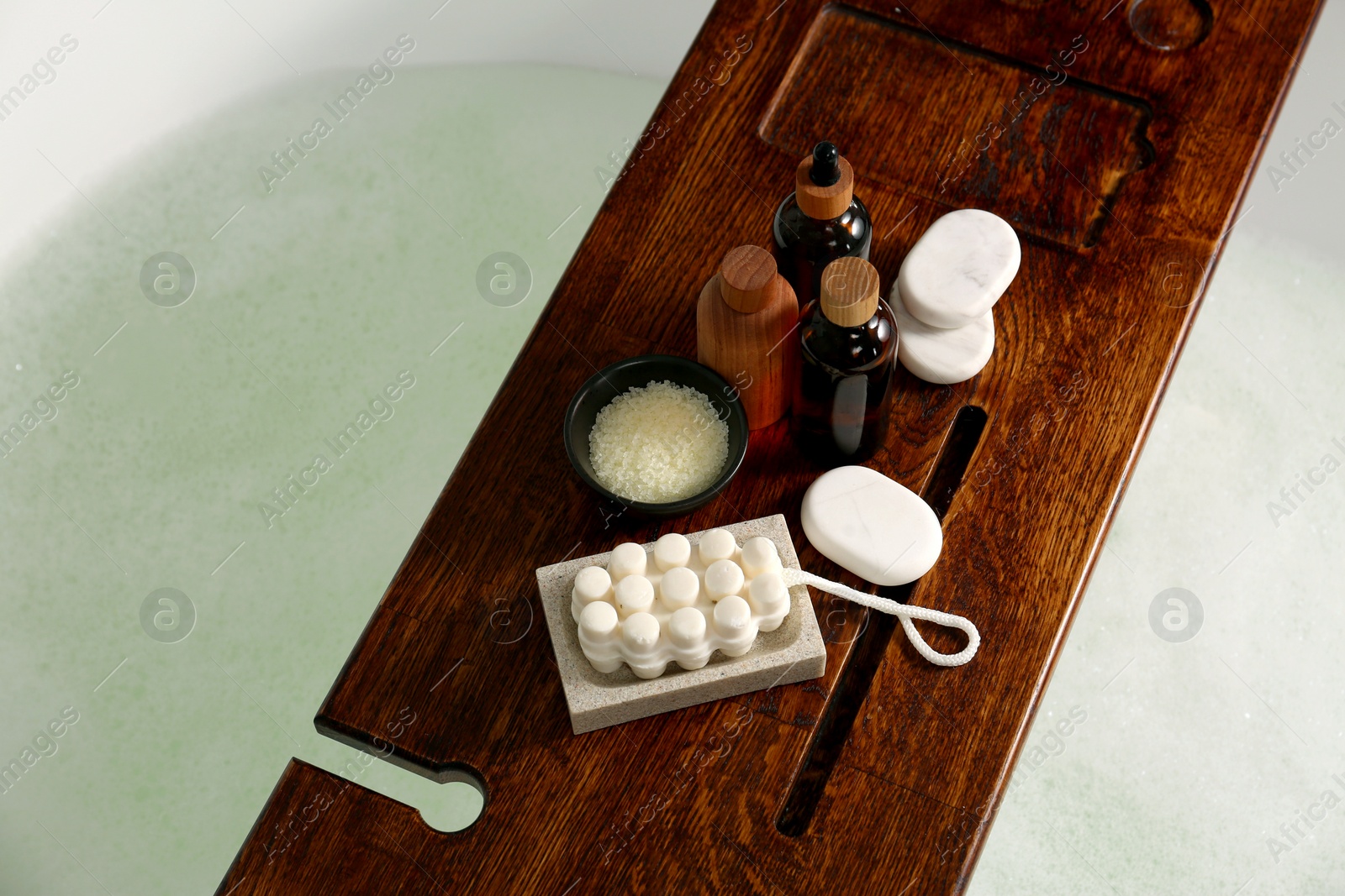 Photo of Wooden board with spa products on bath tub, above view. Space for text