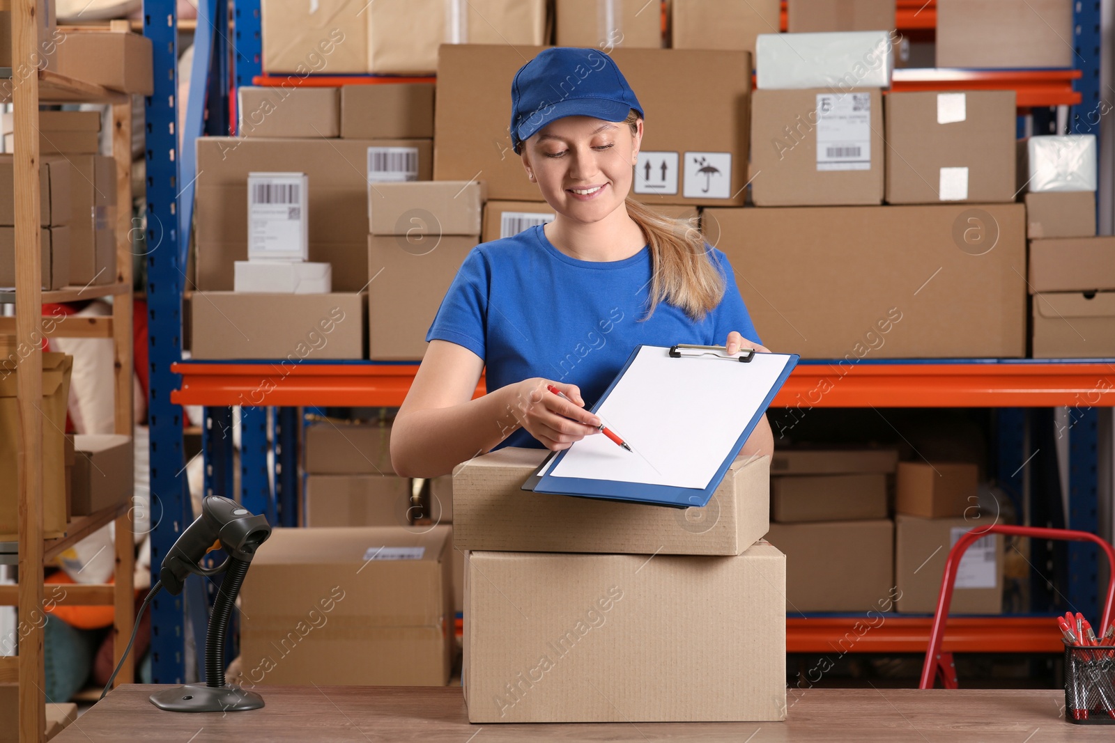 Photo of Post office worker with clipboard and parcels near rack indoors