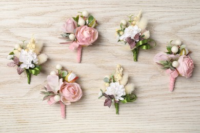 Photo of Stylish boutonnieres on white wooden table, flat lay