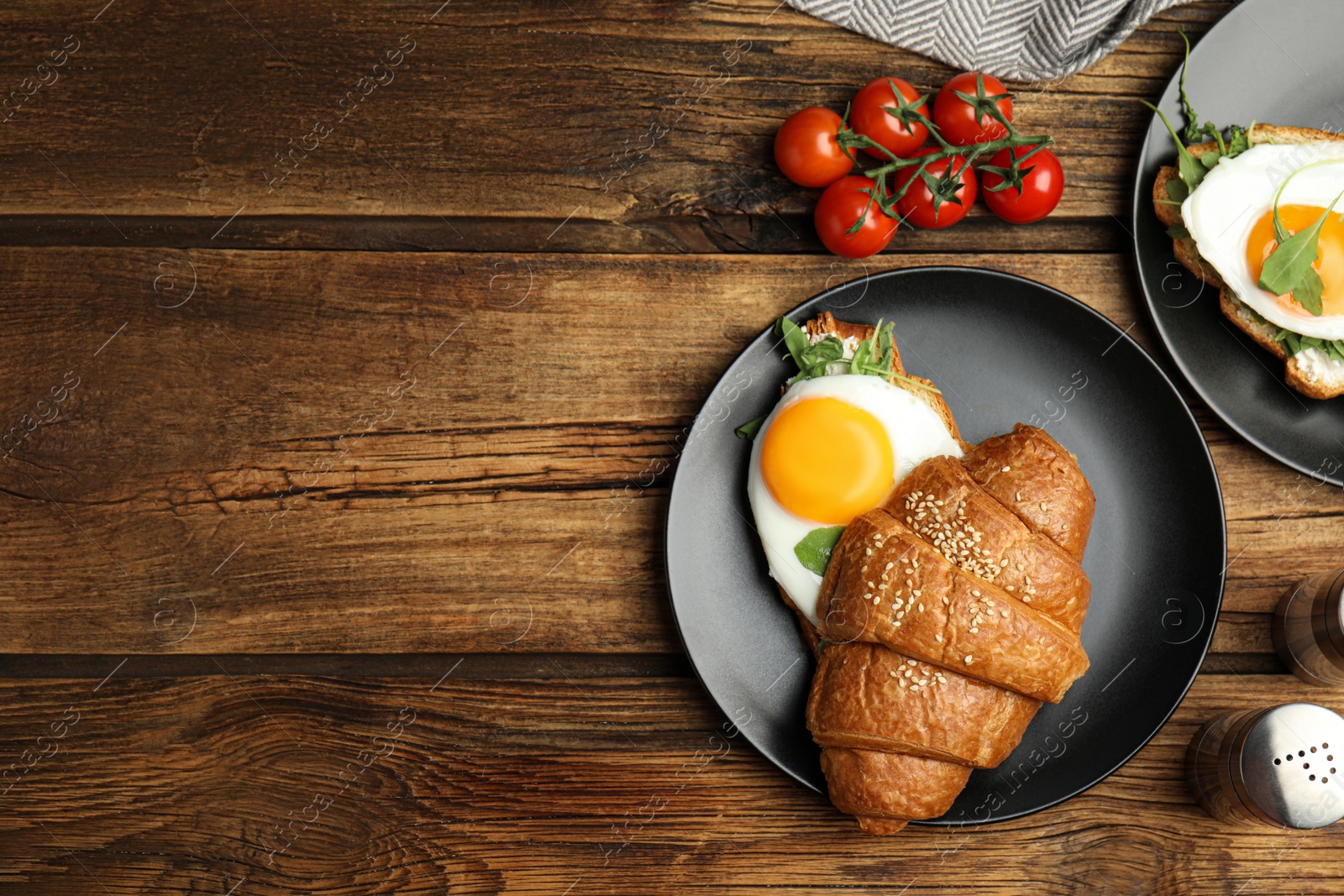 Photo of Delicious croissant with arugula and fried egg on wooden table, flat lay. Space for text