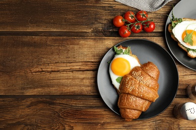 Delicious croissant with arugula and fried egg on wooden table, flat lay. Space for text