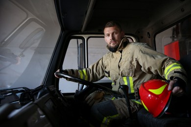 Photo of Firefighter in uniform with helmet driving modern fire truck