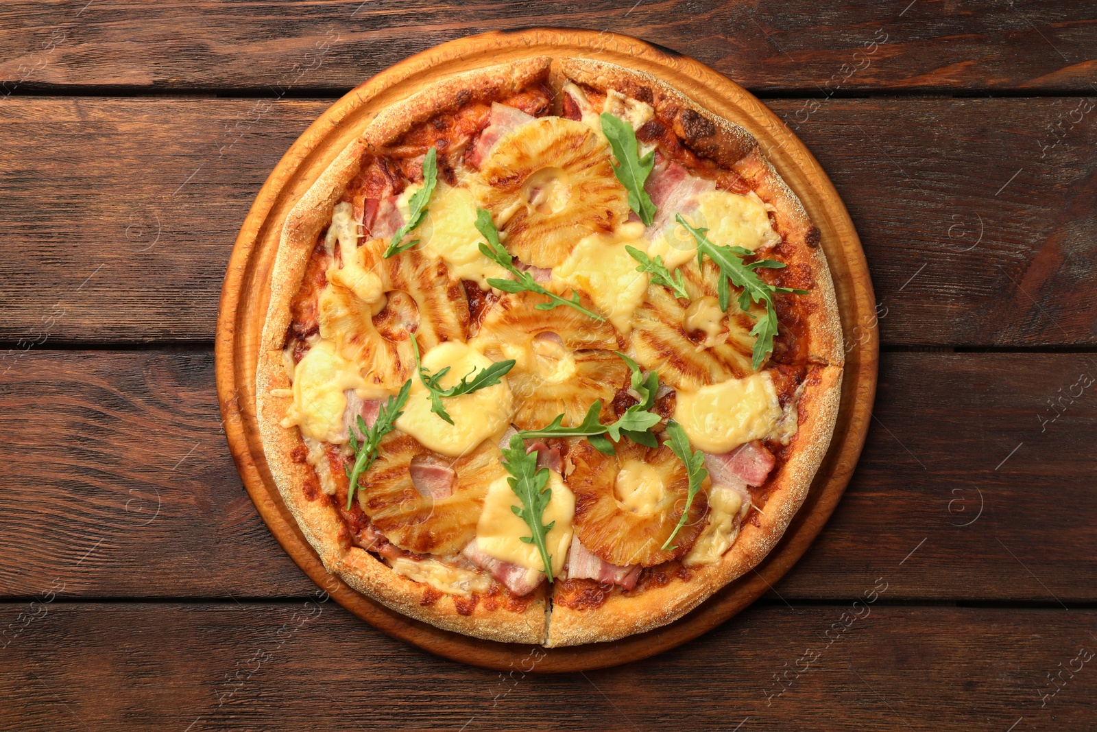 Photo of Delicious pineapple pizza with arugula on wooden table, top view