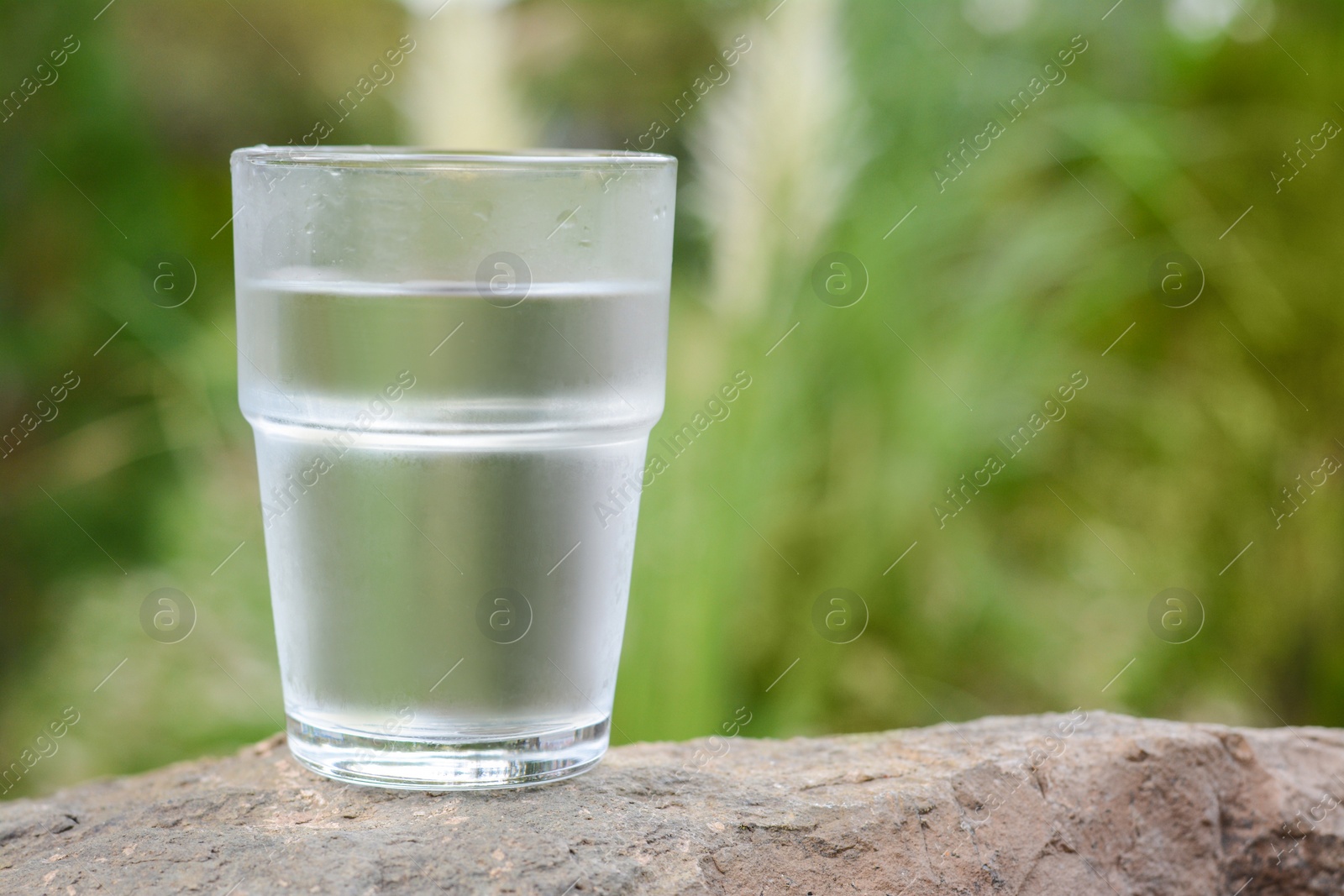 Photo of Full glass of water on stone outdoors, closeup. Space for text