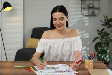 Photo of Young woman coloring antistress page at table indoors