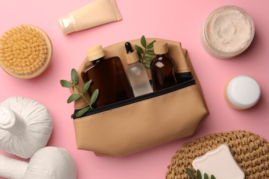 Photo of Preparation for spa. Compact toiletry bag with different cosmetic products and twigs on pink background, flat lay