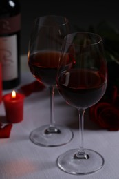 Glasses of red wine, rose flowers and burning candle on white table. Romantic atmosphere