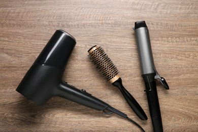 Photo of Curling iron, round brush and hair dryer on wooden background, flat lay
