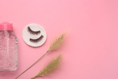 Photo of Bottle of makeup remover, cotton pad, spikelets and false eyelashes on pink background, flat lay. Space for text