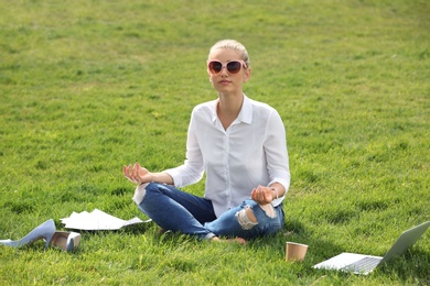 Photo of Young woman meditating on green lawn in park. Joy in moment