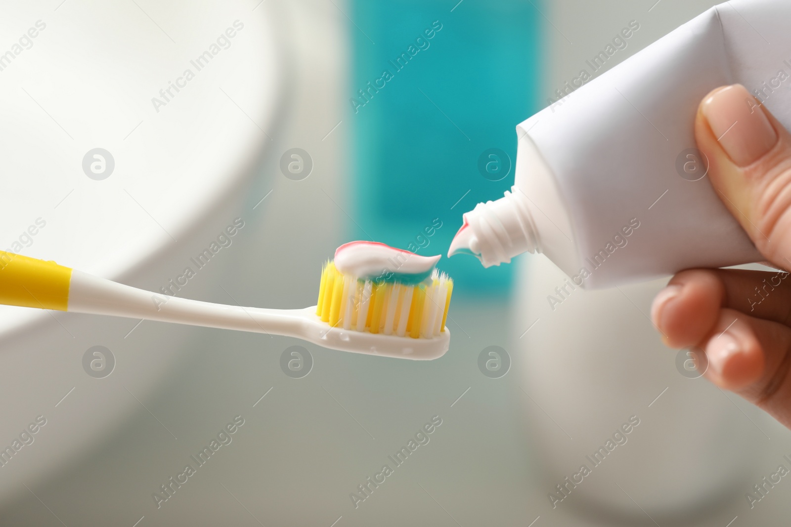 Photo of Woman applying toothpaste on brush against blurred background, closeup