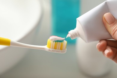 Photo of Woman applying toothpaste on brush against blurred background, closeup