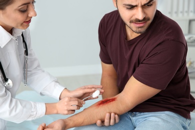 Female doctor cleaning young man's arm injury in clinic. First aid