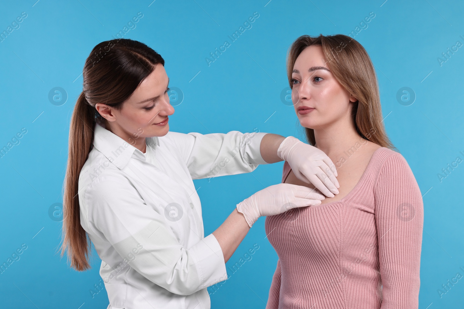 Photo of Mammologist checking woman's breast on light blue background, closeup