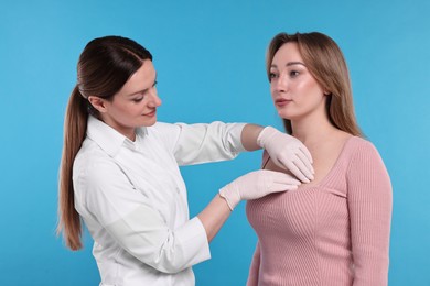 Mammologist checking woman's breast on light blue background, closeup