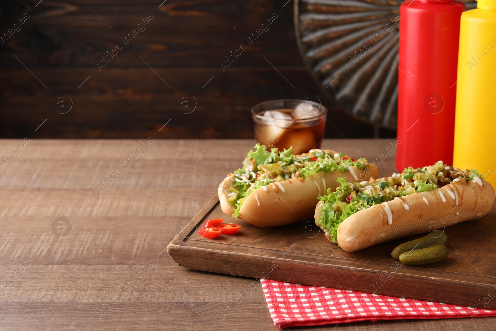 Photo of Tasty hot dogs with chili, lettuce, pickles and sauces on wooden table. Space for text