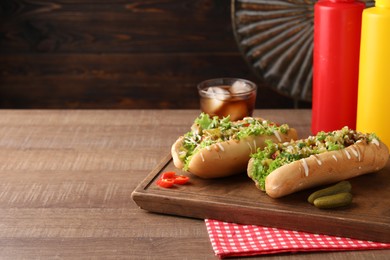 Photo of Tasty hot dogs with chili, lettuce, pickles and sauces on wooden table. Space for text
