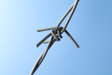 Photo of Metal barbed wire on light blue background, closeup