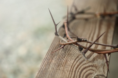 Photo of Crown of thorns on wooden plank against blurred background, closeup with space for text. Easter attribute