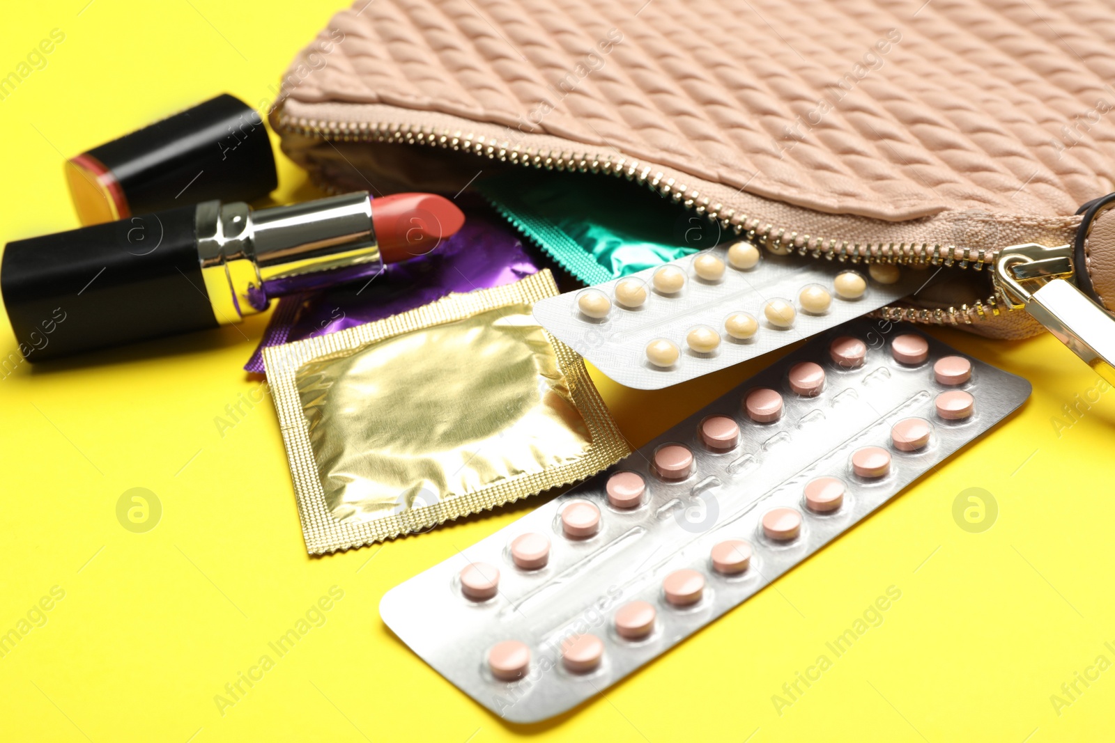 Photo of Different contraceptives and red lipstick near bag on yellow background, closeup. Safe sex concept