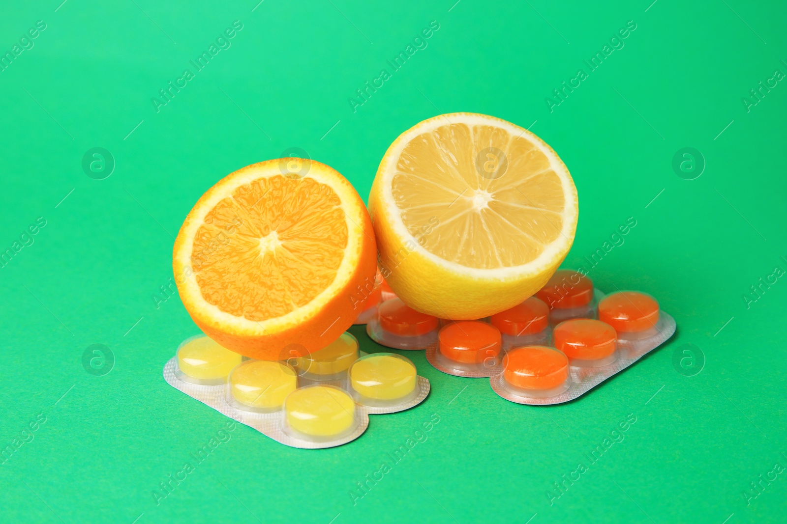 Photo of Blisters with cough drops and fresh fruits on green background