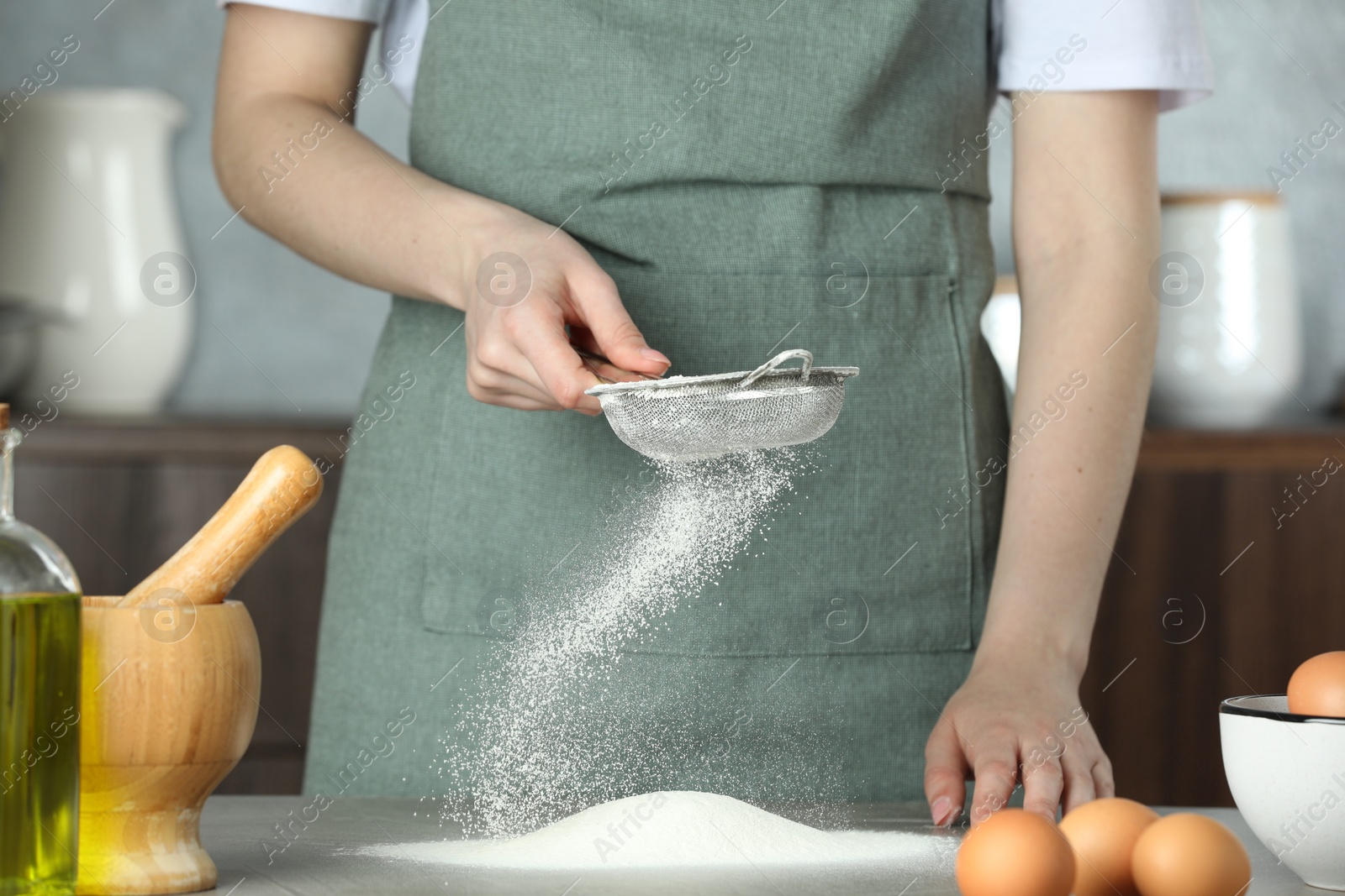 Photo of Woman sieving flour at table in kitchen, closeup