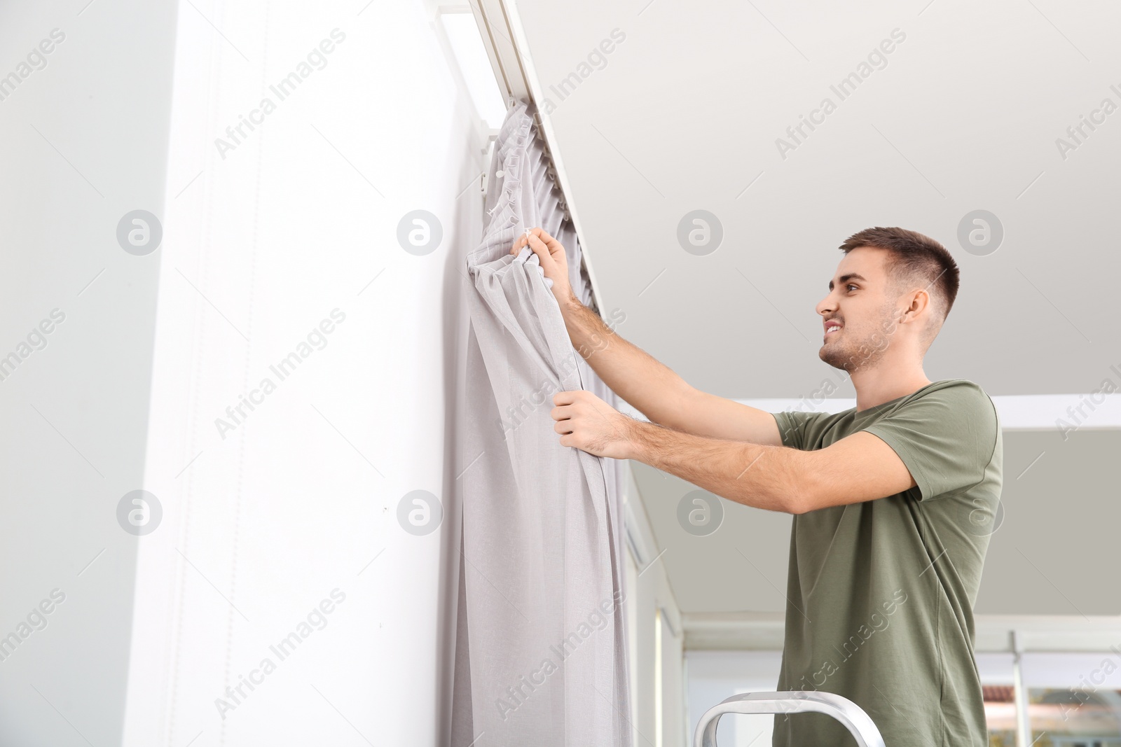 Photo of Man hanging window curtain indoors. Interior decor element