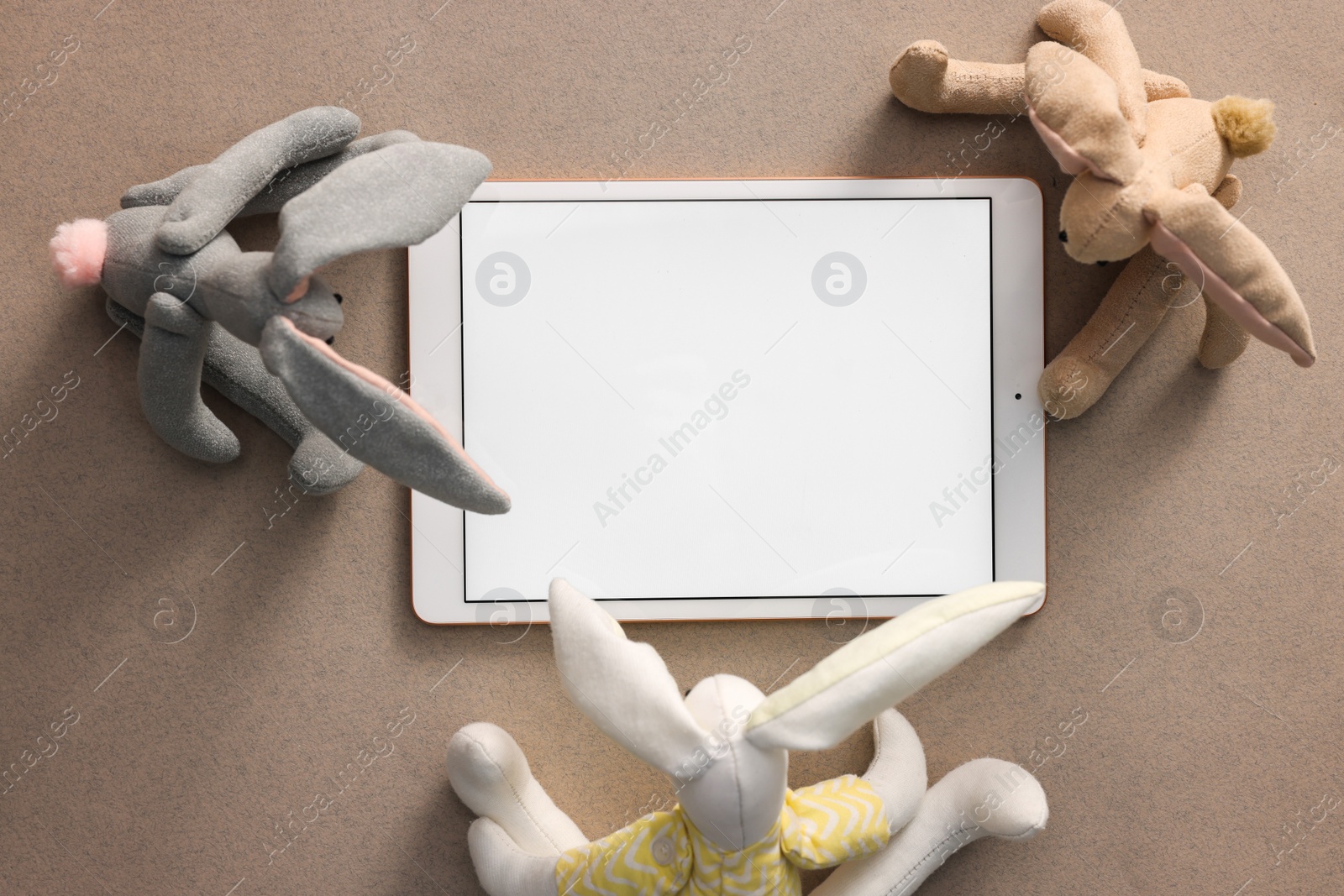 Photo of Modern tablet and kid's toys on light brown background, flat lay. Space for text