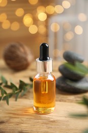 Photo of Essential oil, spa stones and branches of plant on wooden table against blurred lights
