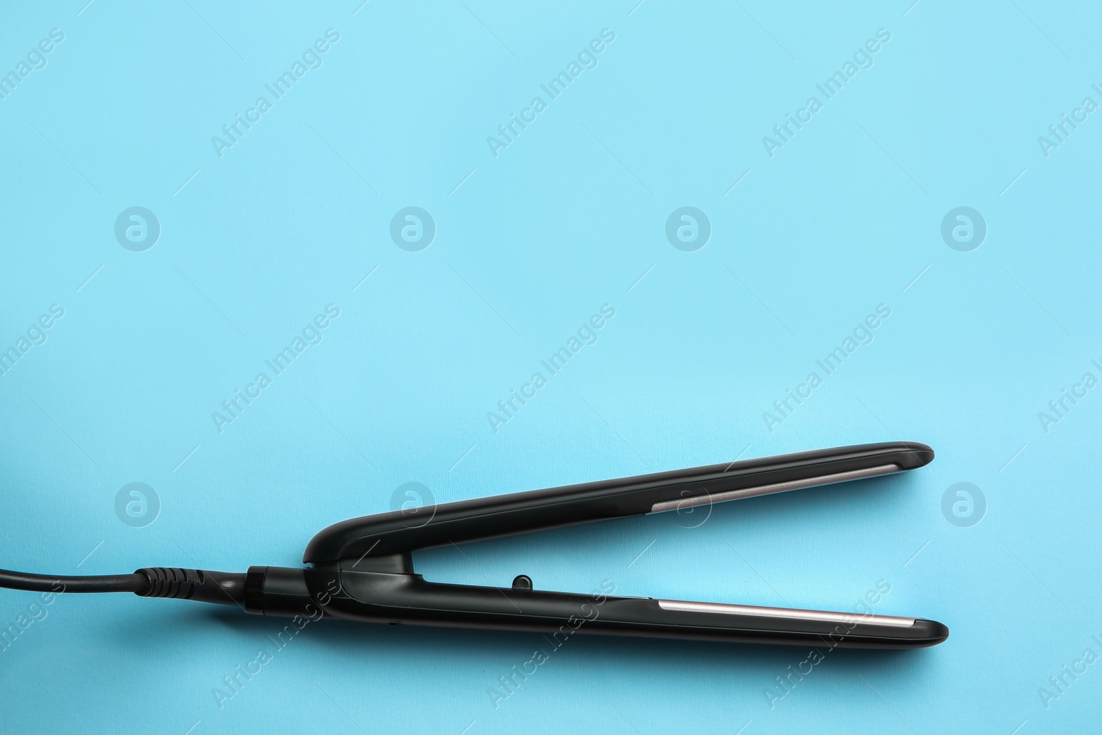 Photo of Modern flat hair iron on light blue background, top view. Space for text