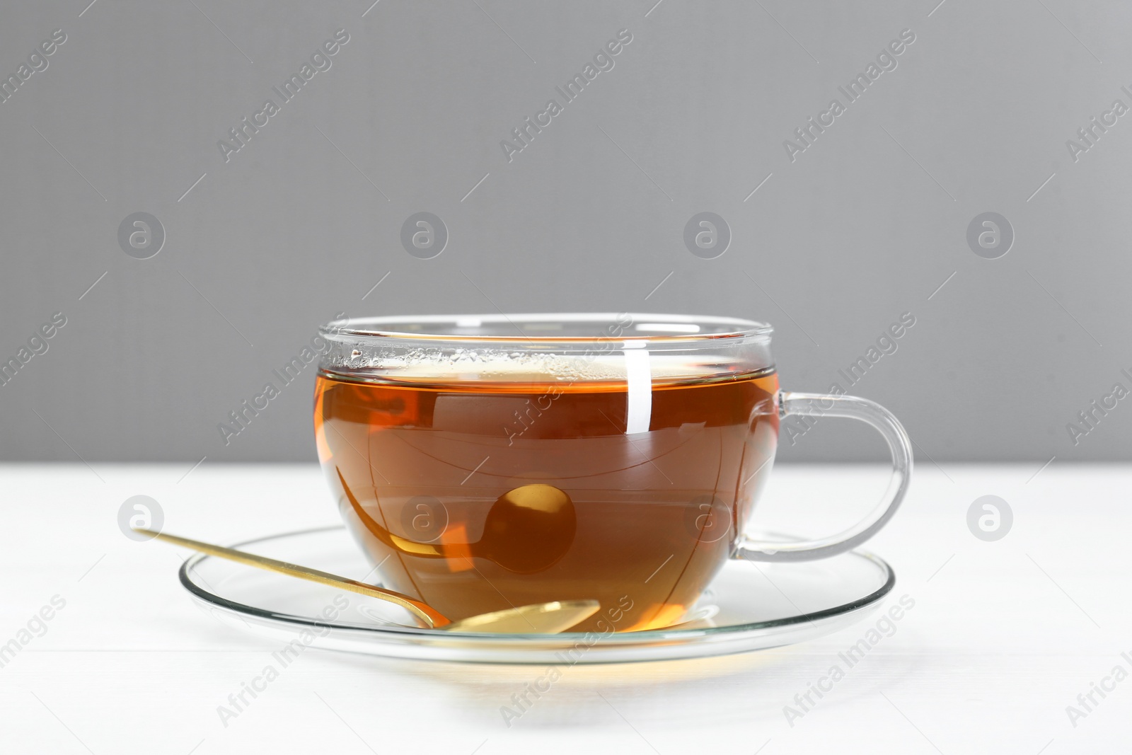 Photo of Glass cup of tea and spoon on white table