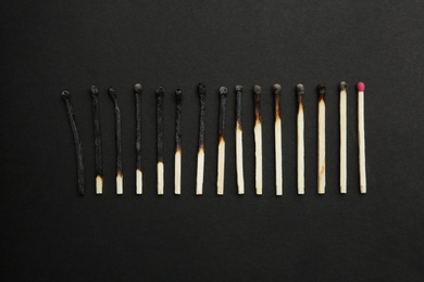 Row of burnt matches and whole one on black background, flat lay. Human life phases concept