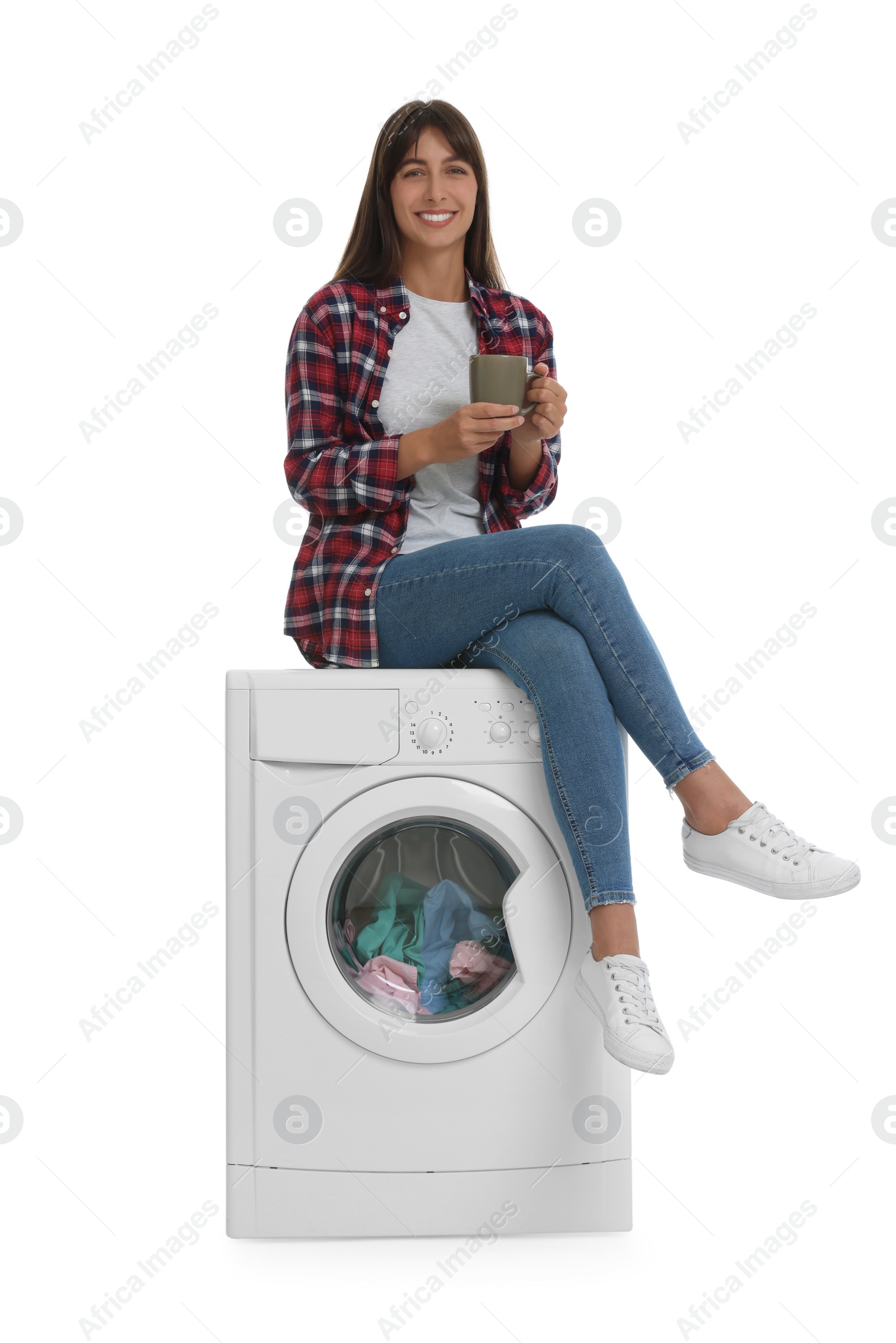 Photo of Beautiful woman with cup of drink sitting on washing machine against white background