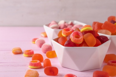 Photo of Bowl of tasty jelly candies on pink wooden table, space for text
