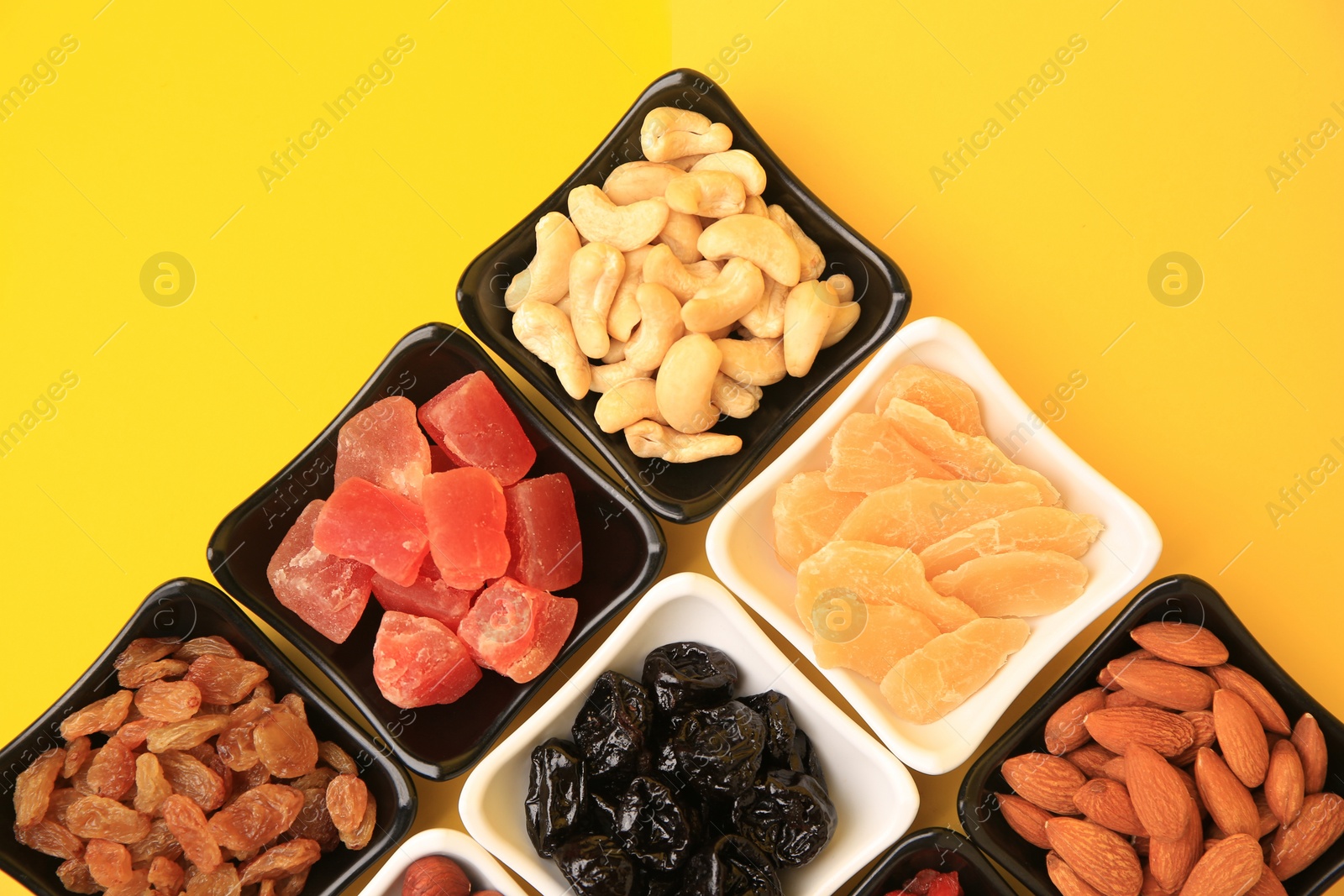 Photo of Bowls with dried fruits and nuts on yellow background, flat lay