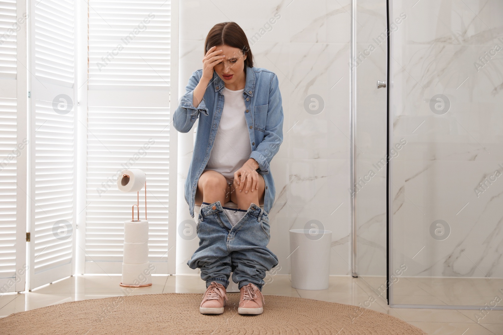 Photo of Woman suffering from hemorrhoid on toilet bowl in rest room