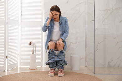 Photo of Woman suffering from hemorrhoid on toilet bowl in rest room