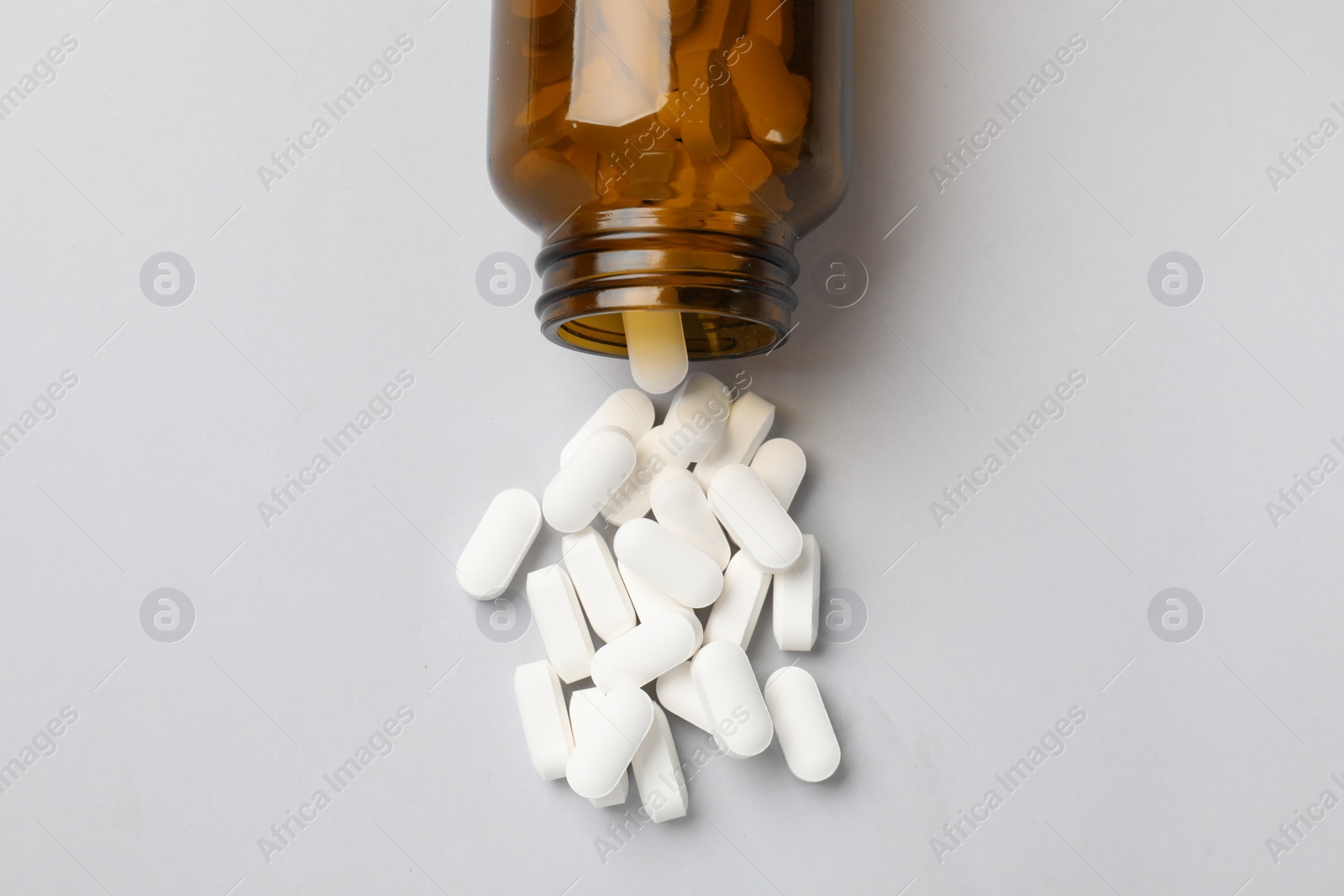 Photo of Vitamin pills and bottle on light grey background, top view