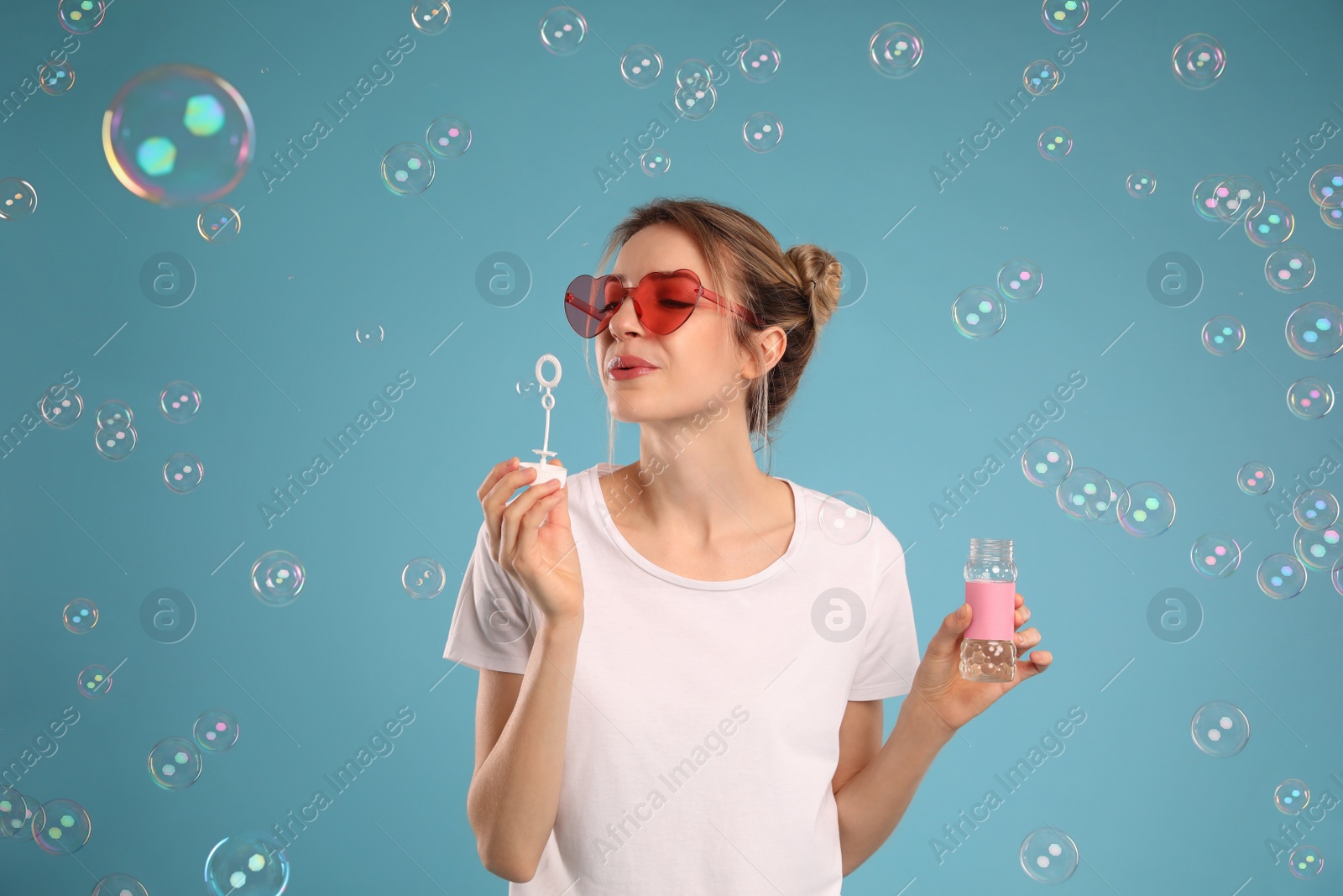 Photo of Young woman blowing soap bubbles on light blue background