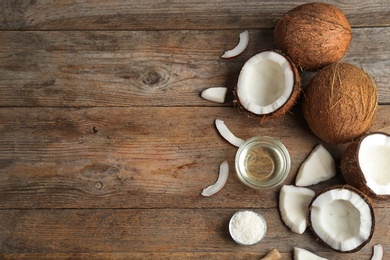 Photo of Bowl of natural organic oil and coconuts on brown wooden background, flat lay. Space for text