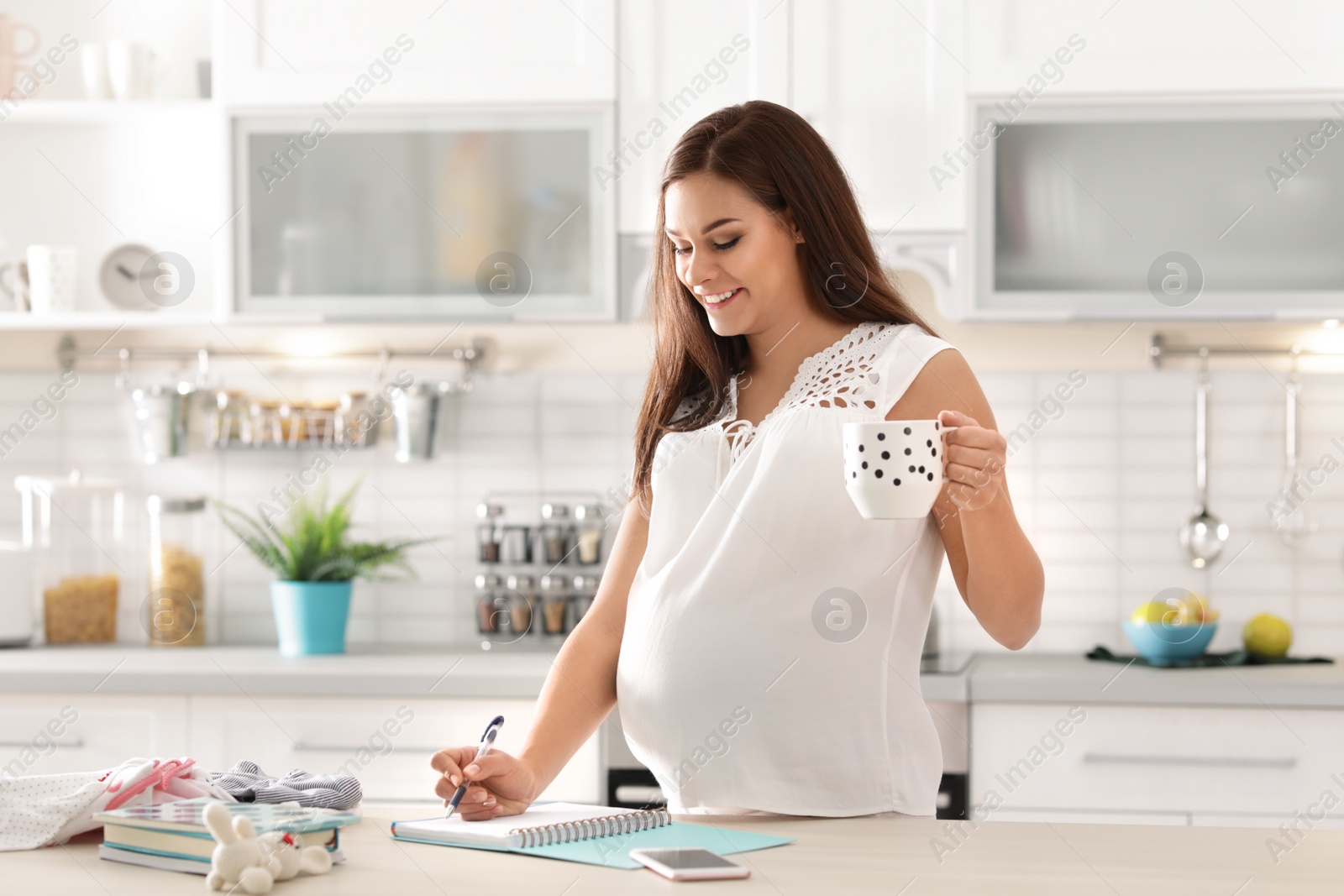 Photo of Pregnant woman writing packing list for maternity hospital in kitchen