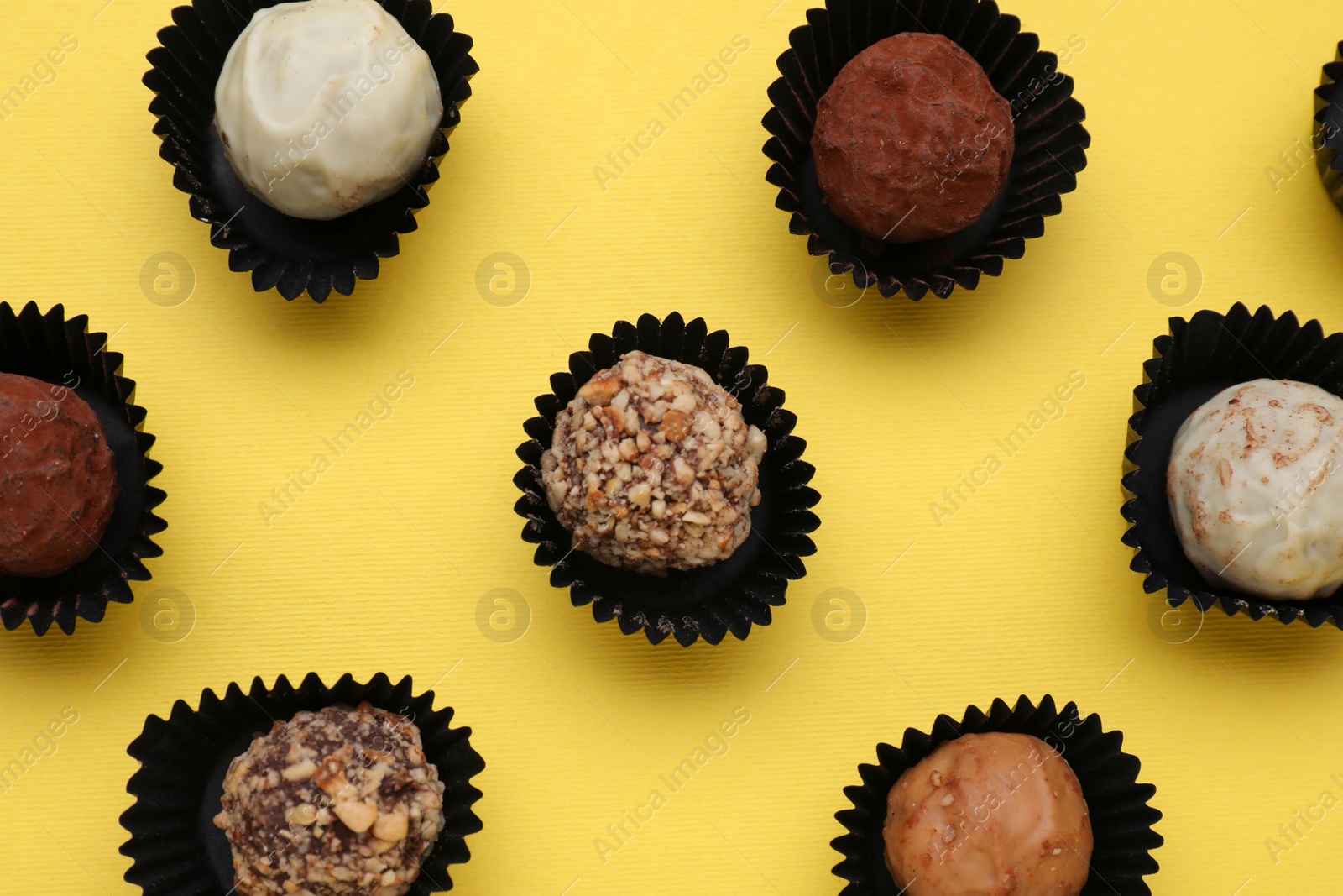 Photo of Different tasty chocolate candies on yellow background, flat lay