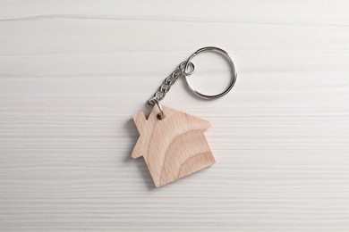 One keychain in shape of house on light wooden table, top view