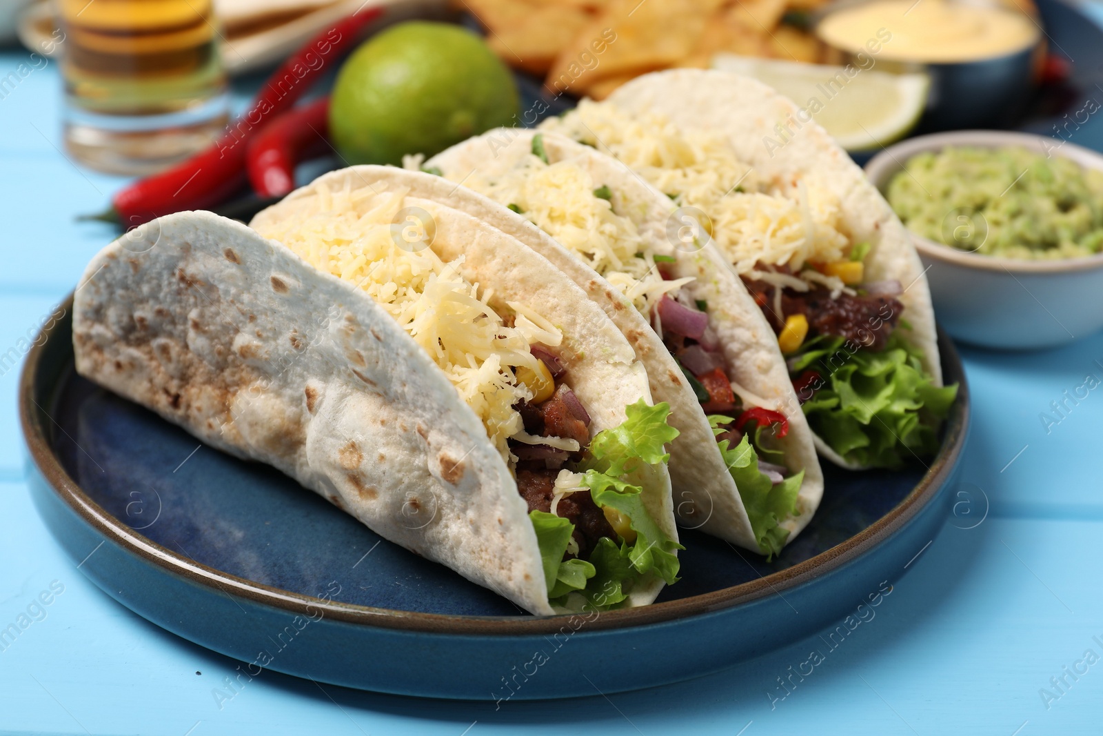 Photo of Delicious tacos with meat and vegetables on light blue table, closeup