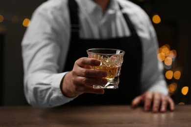 Bartender with glass of whiskey at bar counter indoors, closeup