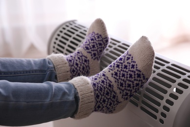 Photo of Child warming feet on electric heater at home, closeup